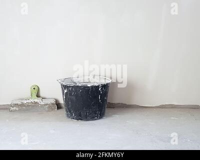 Kitt Messer und Eimer in leerem Raum an der Wand auf Zementboden. Innenhintergrund des Zimmers. Stockfoto