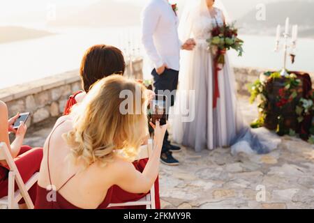 Gäste bei der Hochzeitszeremonie, die Braut und Bräutigam filmten Auf den Telefonen Stockfoto