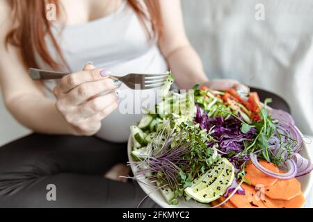 Nahaufnahme eines Tellers mit einem hellen Salat aus frischem Gemüse in den Händen einer Schwangeren. Stockfoto