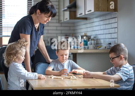 Kleine Kinder spielen Brettspiel mit Holzwürfeln zu Hause in der Küche mit Mama. Stockfoto