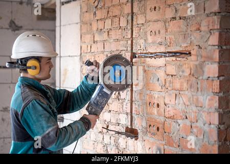 Ein professioneller Baumeister in Arbeitskleidung arbeitet mit einem Schneidwerkzeug. Stockfoto