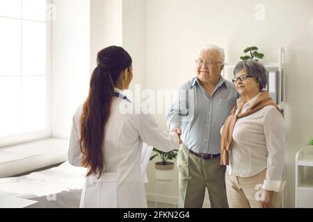 Glückliches Seniorenpaar, das sich bei einem Praktizierenden für die Hilfe und das Schütteln bedankte Hände mit ihr Stockfoto