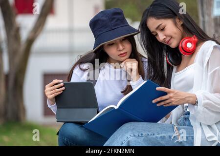 Zwei Studentinnen der Universität studieren im Freien und nutzen zusammen im Park der Universität ein digitales Tablet. Stockfoto