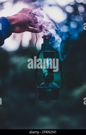 Vertikale Aufnahme der Hand eines Mannes, der eine alte Lampe hält Mit dem Rauch, der aus ihm herauskommt Stockfoto