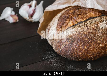 Nahaufnahme von knusprigem Sauerteig-Rundbrot aus Vollkorn in Bastelpackung mit Knoblauch. Natürliche und gesunde Ernährung Konzept. Stockfoto