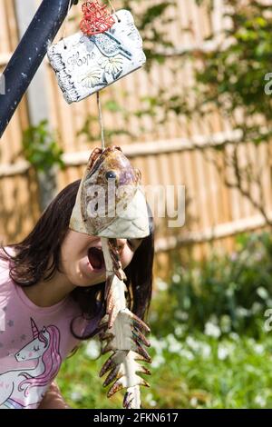 Blick auf ein junges Mädchen in einem Garten mit Spaß Vorgeben, einen baumelnden Keramikfisch zu essen Stockfoto