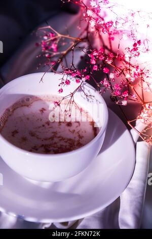 Weiße Tasse Milch und Schokolade. Morgenstimmung. Frühstück. Rosa Gypsophila Blüten Stockfoto