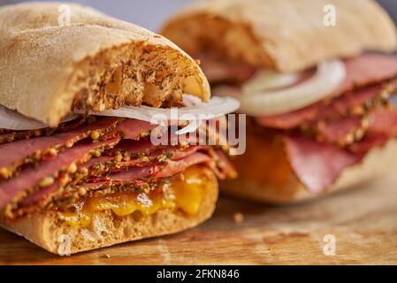 Dünn geschnittener Pastrami-Sand, der sich mit köstlichen Speisen auf Baguette-Brot mit Käsekäse, Zwiebeln trifft Stockfoto