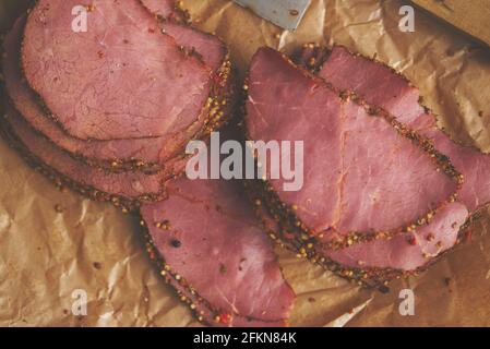 Köstliche Pastrami-Scheiben aus gebratenem Rindfleisch auf Papier mit Körnern Von farbigem Pfeffer Stockfoto