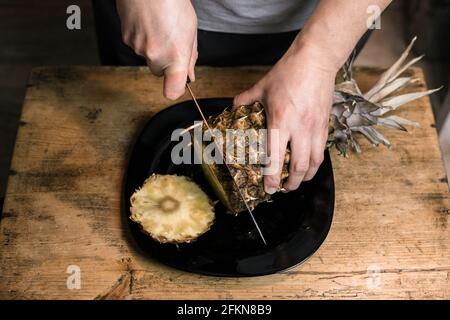 Man schneidet Ananas mit einem Messer auf einem Holztisch Stockfoto