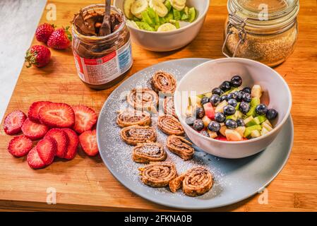 Schokoladen-Haselnussaufstrich oder Nutella-Crepe-Brötchen mit frischen Früchten wie Erdbeeren, Kiwi, Banane und Blaubeeren auf rustikalem Holzbrett Stockfoto