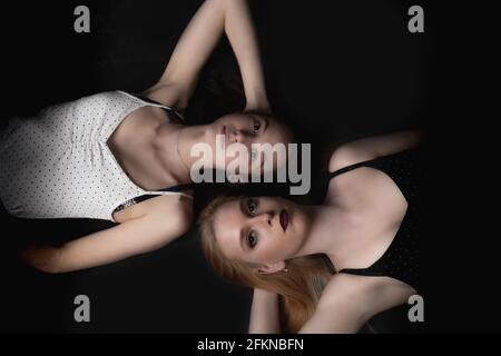 Zwei junge Frauen liegen auf dem schwarzen Boden und schauen auf die Kamera. Horizontal. Stockfoto