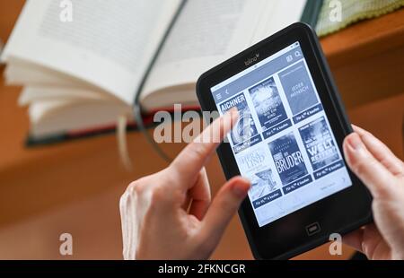 Berlin, Deutschland. April 2021. ILLUSTRATION - EINE Frau hält einen eBook Reader in den Händen und betrachtet die Auswahl aktueller Bücher. Im Hintergrund ein gedrucktes Buch. Quelle: Jens Kalaene/dpa-Zentralbild/ZB/dpa/Alamy Live News Stockfoto