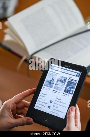 Berlin, Deutschland. April 2021. ILLUSTRATION - EINE Frau hält einen eBook Reader in den Händen und betrachtet Empfehlungen aktueller Bücher. Im Hintergrund ein gedrucktes Buch. Quelle: Jens Kalaene/dpa-Zentralbild/ZB/dpa/Alamy Live News Stockfoto