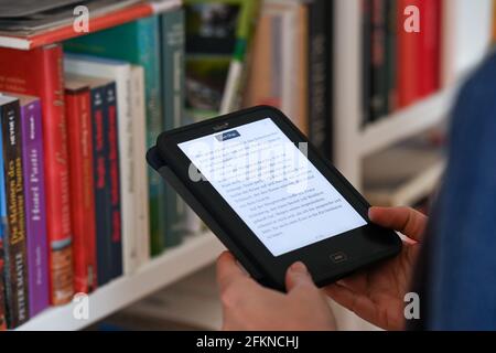 Berlin, Deutschland. April 2021. ILLUSTRATION - EINE Frau hält einen eBook Reader in den Händen. Im Hintergrund gedruckte Bücher auf einem Bücherregal. Quelle: Jens Kalaene/dpa-Zentralbild/ZB/dpa/Alamy Live News Stockfoto