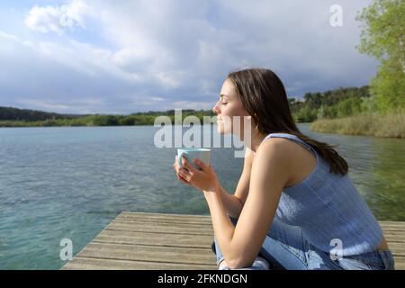 Profil einer Frau, die sich beim Kaffeetrinken in einem See entspannt pier Stockfoto