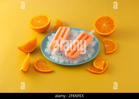 Orangefarbene Eiszapfen auf blauer Platte auf gelbem Hintergrund Stockfoto