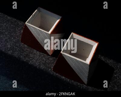 Leere DIY Betontöpfe, Pyramidenform auf dunklem Hintergrund, Draufsicht. Zwei einzigartige kupferfarben lackierte Zementpflanzer. Stockfoto