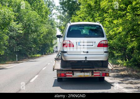 LKW-Transporter mit Auto auf der Straße. Rückansicht. Leuchtend grüne Bäume entlang der Straße Stockfoto