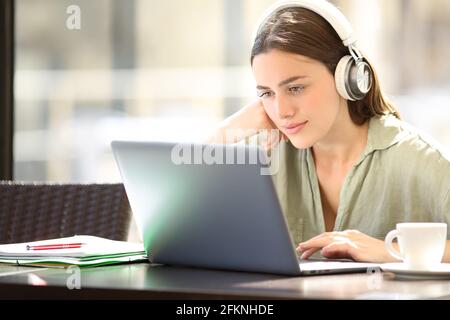 Zufriedene Frau e-Learning mit Laptop und Kopfhörer sitzen in einem Bar Stockfoto