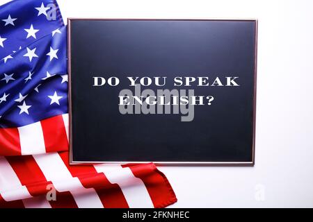 Nahaufnahme der schwarzen Tafel mit der Frage Sprechen sie Englisch? Geschrieben, zerzauste USA-Flagge und weiße Textstelle. American English CO Stockfoto