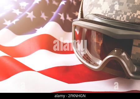 US Army Kevlar Kampfhelm, Camoabdeckung, taktische Brille, USA Flagge Hintergrund. Memorial Weekend, Veteranentag, United States of America Armed Forces Stockfoto