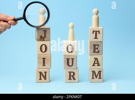 Holzfiguren von Männern stehen auf Würfeln mit der Inschrift und einer Hand mit einer Lupe auf blauem Hintergrund. Rekrutierungskonzept, Suche nach t Stockfoto