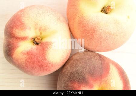 Drei reife süße, natürliche Pfirsiche, aus der Nähe, auf einem bemalten Holztisch. Stockfoto