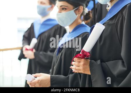 Seitenansicht einer Gruppe junger Menschen mit Abschlussfeier Kleider und Masken, während sie in Reihe stehen Stockfoto