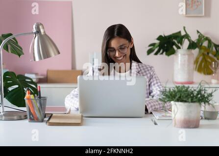 Glückliche junge indische Mixed-Race-Geschäftsfrau mit Computer Blick auf Der Bildschirm, der im Internet funktioniert, sitzt am Schreibtisch Stockfoto