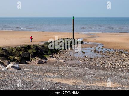 Eine einone Figur, die in Richtung der fernen Flut geht, an der Meeresabwehr am Rossall-Strand Stockfoto