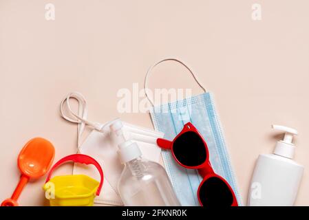 Schützende OP-Maske, Schutzmaske ffp2 KN95 mit Sonnenbrille, Strandeimer und Plastikflasche Sonnencreme auf beigem Hintergrund.Sommerkonzept Stockfoto