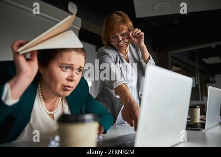 Strikter CEO, der Fehler auf dem Laptop eines verärgerten Mitarbeiters bemerkt Stockfoto