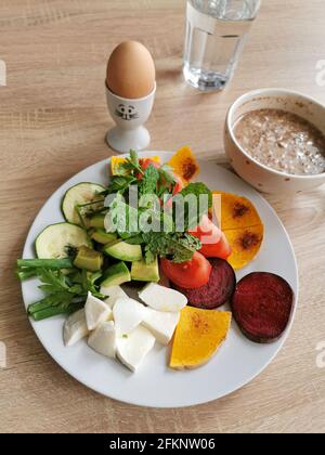 Ein gesundes Frühstück, das reich an Proteinen, Fetten und Kohlenhydraten ist. Haferflocken mit Nüssen, weich gekochtes Ei, Mocarella-Käse, buntes Gemüse Stockfoto