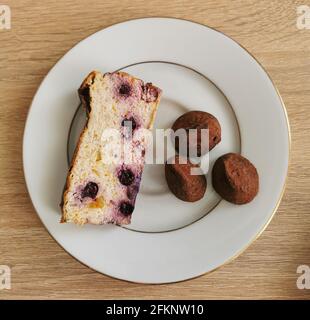 Ein Stück hausgemachter Käsekuchen mit Heidelbeeren und drei süßen Trüffel auf einem weißen Teller Stockfoto