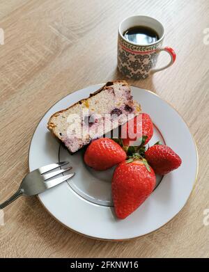 Ein Stück hausgemachter Käsekuchen mit Heidelbeeren, Erdbeeren auf einem weißen Teller und Kaffee Stockfoto