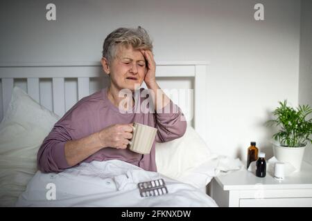 Kranke ältere Frau im Bett zu Hause, Kopfschmerzen und Krankheit Konzept. Stockfoto