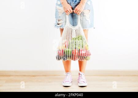 Junge Frau im karierten Hemd, Jeansrock mit Beutel mit gemischtem Obst, Gemüse & Gemüse: Maiskolben, Tomaten, Pfeffer, Salat, Birne & Apfel. Zero Waste Konz Stockfoto