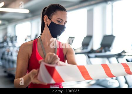 Fitnesstrainer mit Gesichtsmaske zur Markierung sicherer Entfernung im Fitnessstudio, Coronavirus-Konzept. Stockfoto