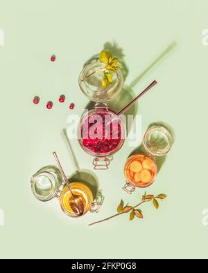 Gärung und Lagerung von Obst, Gemüse und Beeren. Lebensmittelzusammensetzung mit Glasgläsern mit fermentiertem Honig, Preiselbeeren, Zitrone und Karotte auf Minze Stockfoto
