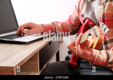 Musik Hochschule Hipster Student in kariertem kariertem kariertem Hemd üben E-Gitarre Übung, Lesen von Notizen, pc-Laptop-Computer. Der Mensch lehrt sich selbst, t Stockfoto