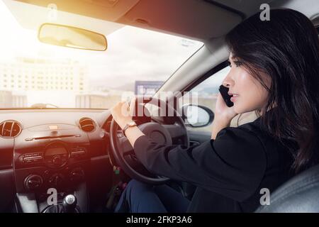 Schöne asiatische Frau tragen schwarzen Anzug Arbeitskleidung reden auf einem Mobiltelefon im Auto in der Abendzeit auf Sonnenlicht Hintergrund. Stockfoto
