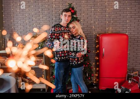 Ein Kerl mit einem Mädchen in einem Pullover und Jeans umarmen, küssen und halten Wunderkerzen in den Händen Stockfoto