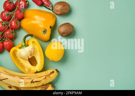 Sortiment aus frischem Pfeffer, Chili, Bananen, Kirschtomaten, Zitrone und Kiwi in Bastelpapiertüte auf grünem Hintergrund. Trendy hässlich Bio-Gemüse und Stockfoto