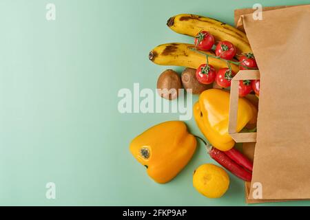 Sortiment aus frischem Pfeffer, Chili, Bananen, Kirschtomaten, Zitrone und Kiwi in Bastelpapiertüte auf grünem Hintergrund. Trendy hässlich Bio-Gemüse und Stockfoto