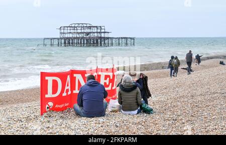 Brighton UK 3. Mai 2021 - EINE Familie versucht, etwas Schutz hinter einem Gefahrenspruchband am Brighton Strand zu bekommen, während Besucher trotz des windigen Wetters die Maifeiertage genießen : Credit Simon Dack / Alamy Live News Stockfoto