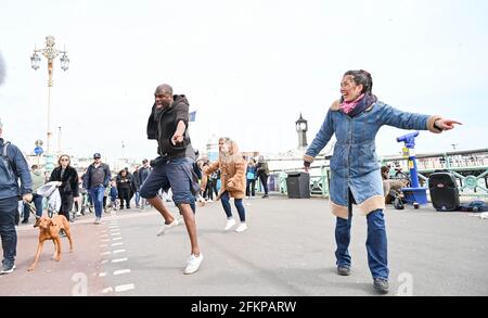 Brighton UK 3. Mai 2021 - Dancing in the Street on Brighton Seafront as visitors enjoy the May Bank Holiday trotz des windigen Wetters : Credit Simon Dack / Alamy Live News Stockfoto