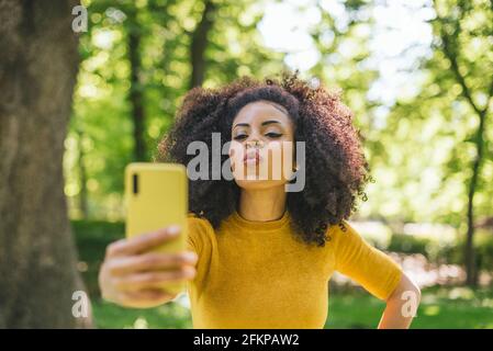 Hübsche Afro-Frau, die ein Selfie mit einem Kuss nimmt. Stockfoto