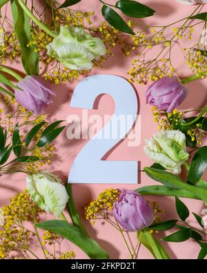 Nummer zwei auf rosa Hintergrund mit bunten Blumen. Flach liegend, Draufsicht. Stockfoto