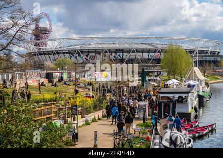 LONDON, Großbritannien - 11. APRIL 2021: Menschen vor den Grachtenbars in Hackney Wick in London an einem sonnigen Tag. Im Hintergrund sieht man das West Ham Stadium. Stockfoto